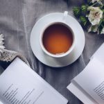 Japanese Tea Poetry - White Ceramic Teacup With Saucer Near Two Books Above Gray Floral Textile